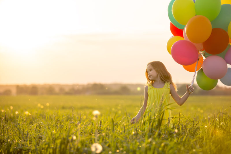 dziewczynka trzymająca kolorowe balony, spacerująca po łące